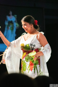 Designer Adria Renee toasts the crowd with a margarita, wearing her Jurassic Park-inspired design on the runway of the Her Universe Fashion Show. 