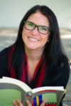 Photo is a headshot of Emily, creator of Portrait of a Fangirl, holding up a college text book