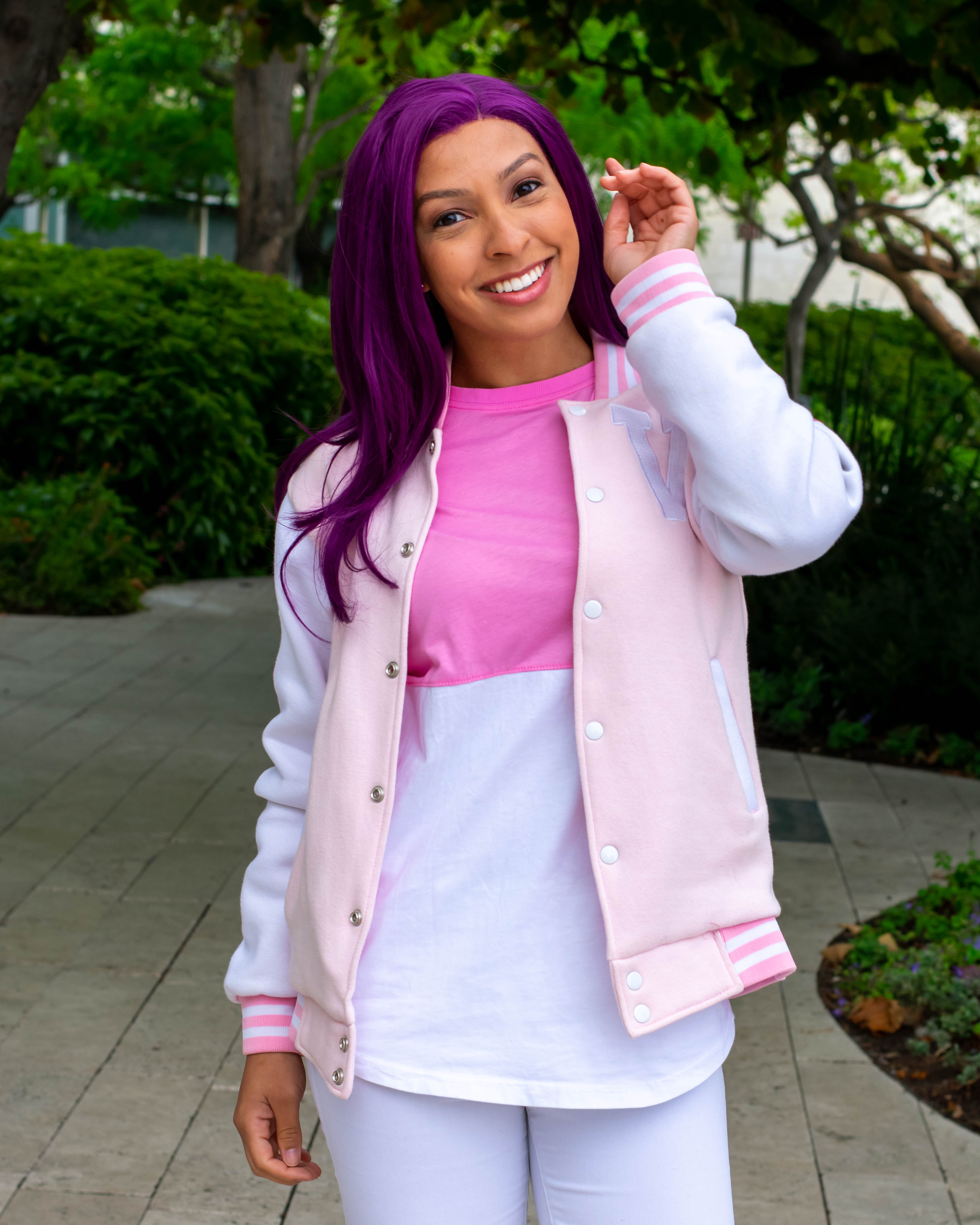 Utahime Cosplay pictured in a pink Voltron shirt. She is standing in a courtyard with trees and bushes behind her