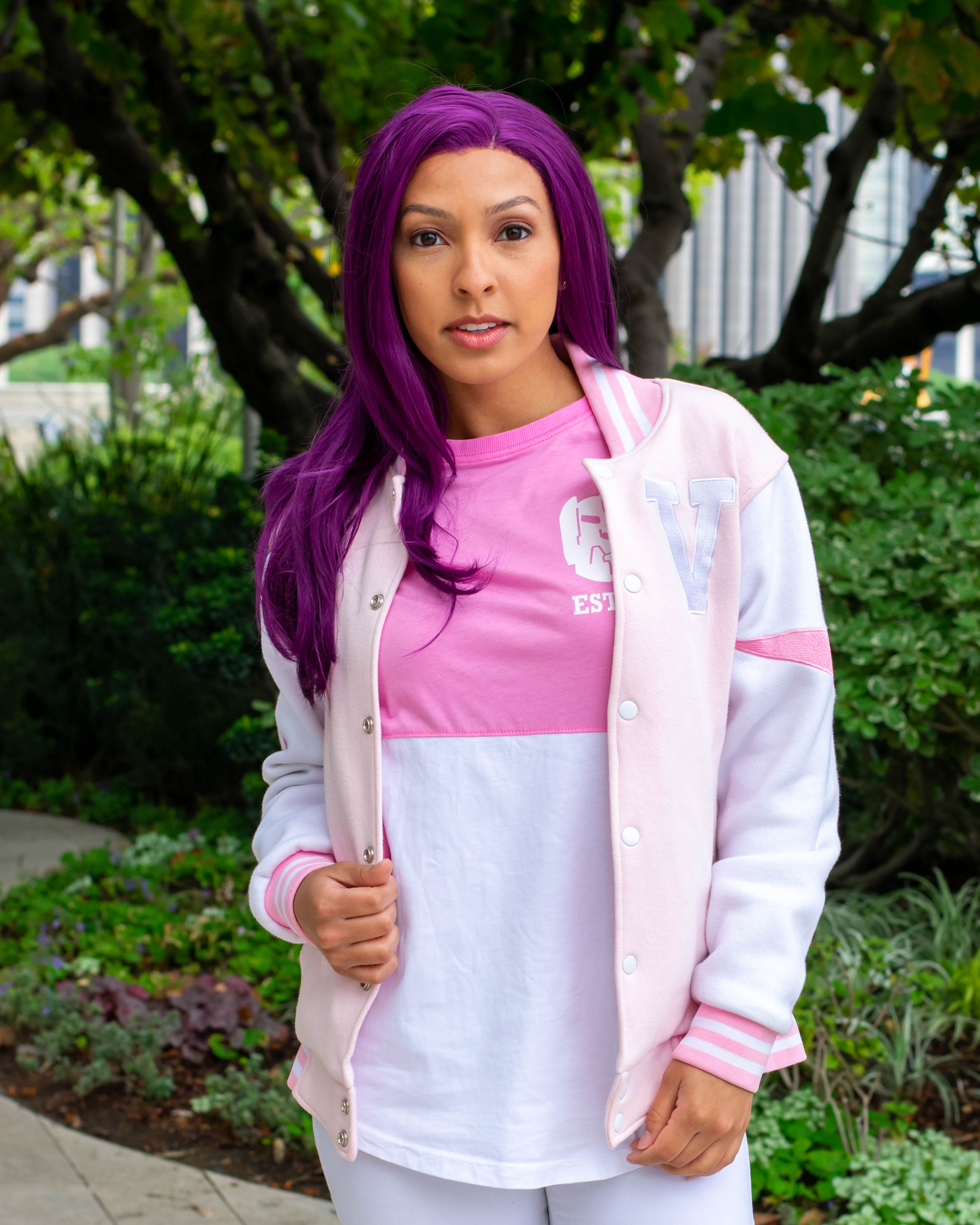 Utahime Cosplay pictured in a pink Voltron shirt. She is standing in a courtyard with trees and bushes behind her