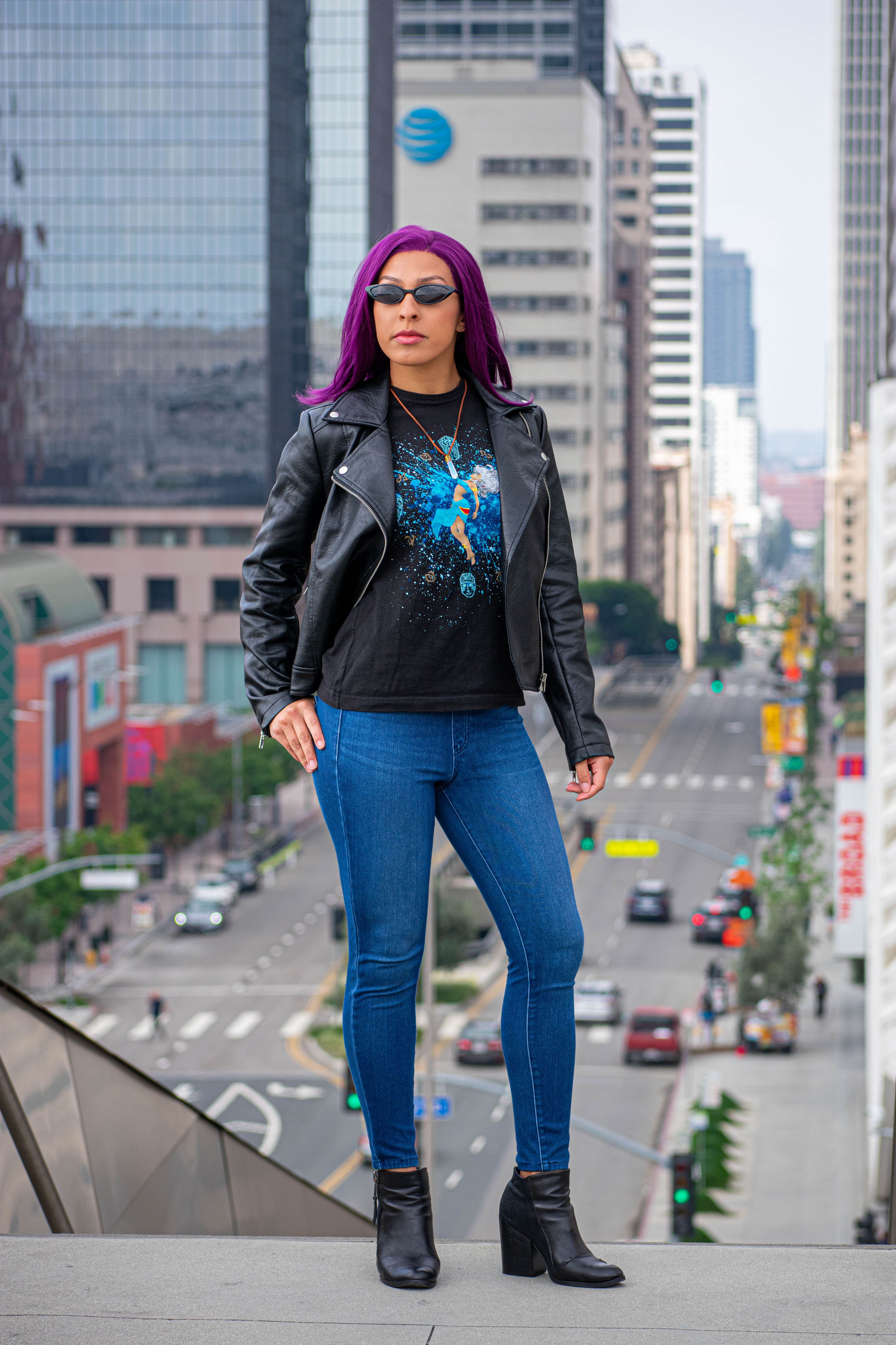 Utahime Cosplay pictured in a Kida inspired Tee Shirt and crystal necklace. She is wearing jeans and a black leather jacket. The Los Angeles Skyline is visible behind her.