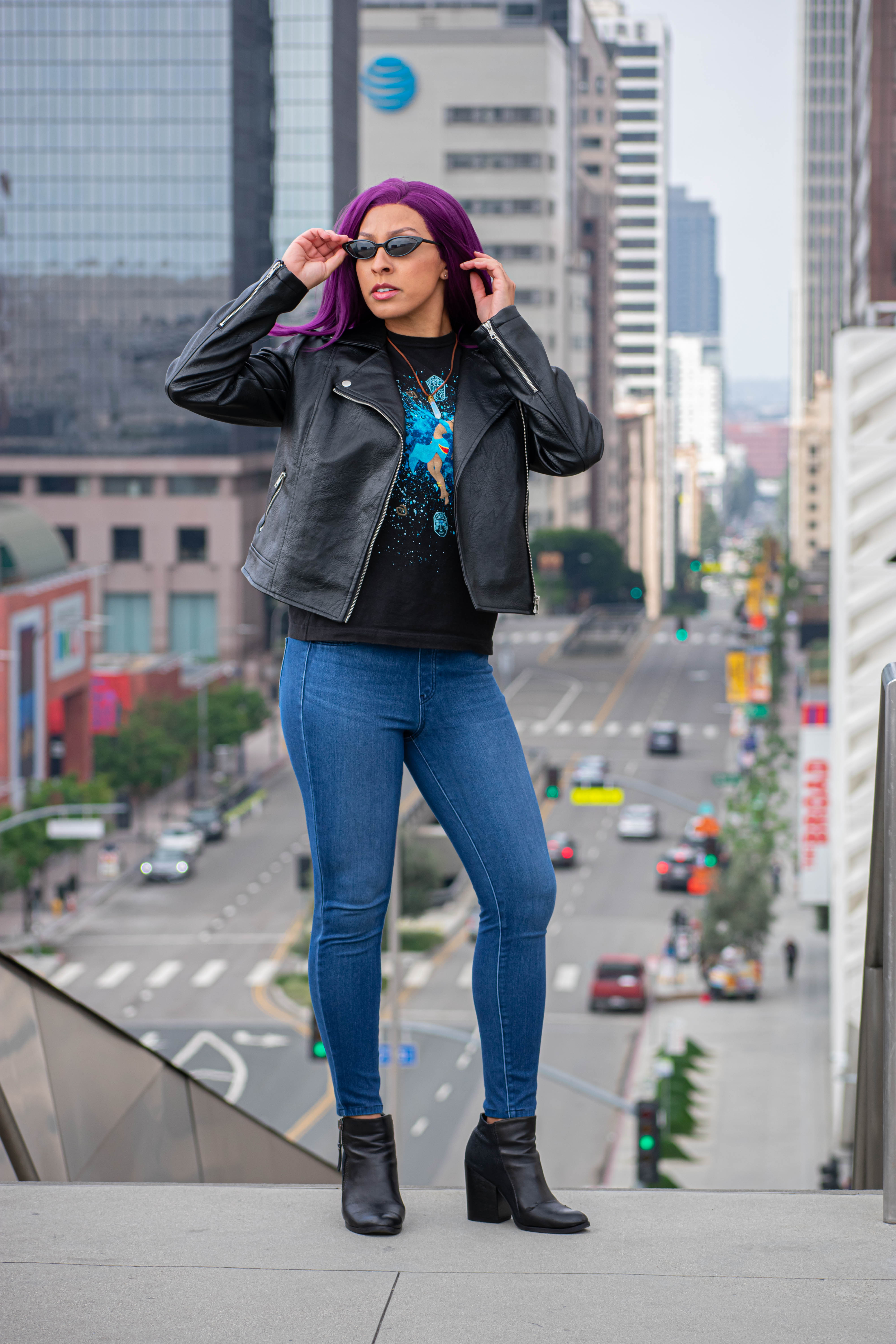 Utahime Cosplay pictured in a Kida inspired Tee Shirt and crystal necklace. She is wearing jeans and a black leather jacket. The Los Angeles Skyline is visible behind her.