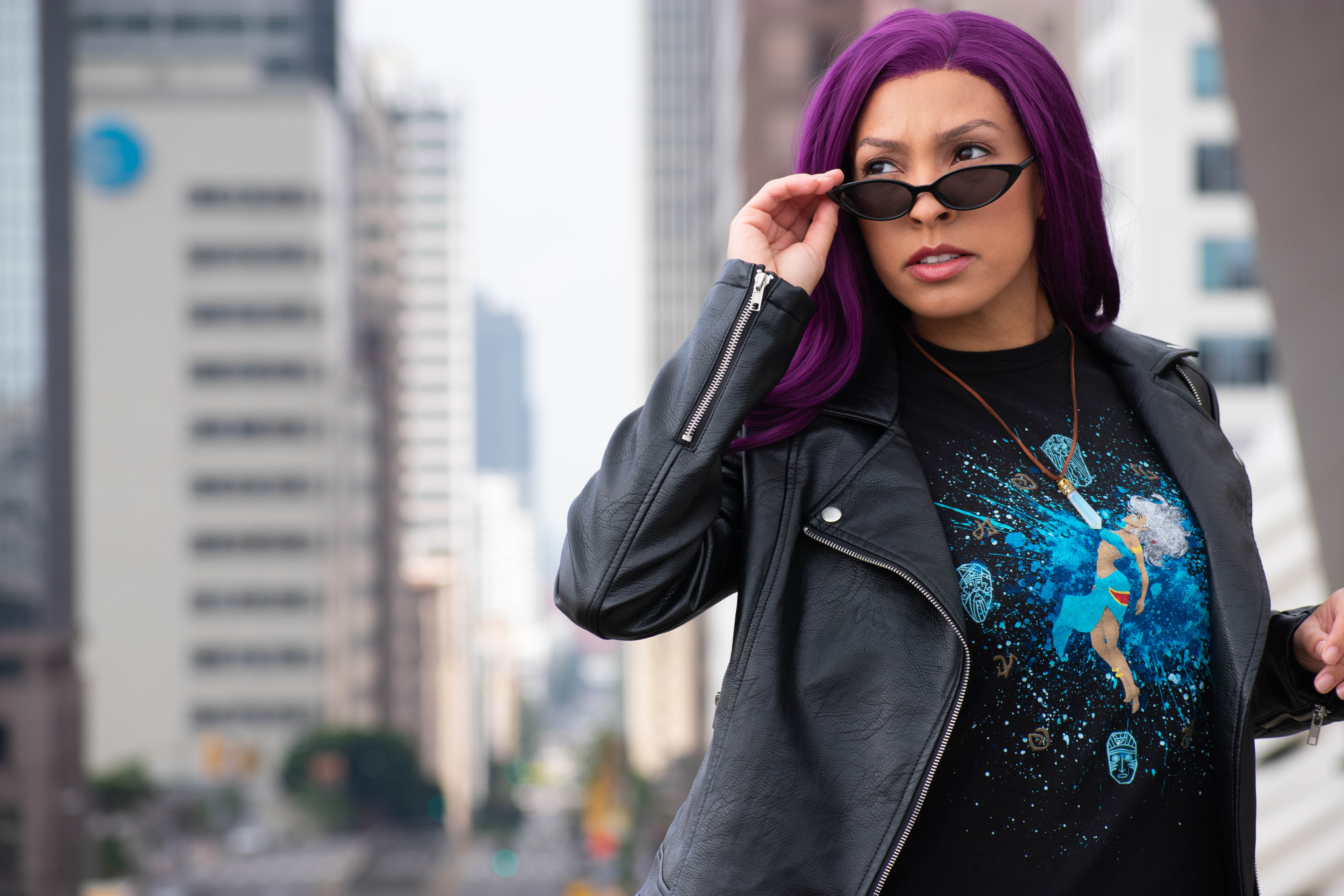 Utahime Cosplay pictured in a Kida inspired Tee Shirt and crystal necklace. She is wearing jeans and a black leather jacket. The Los Angeles Skyline is visible behind her.