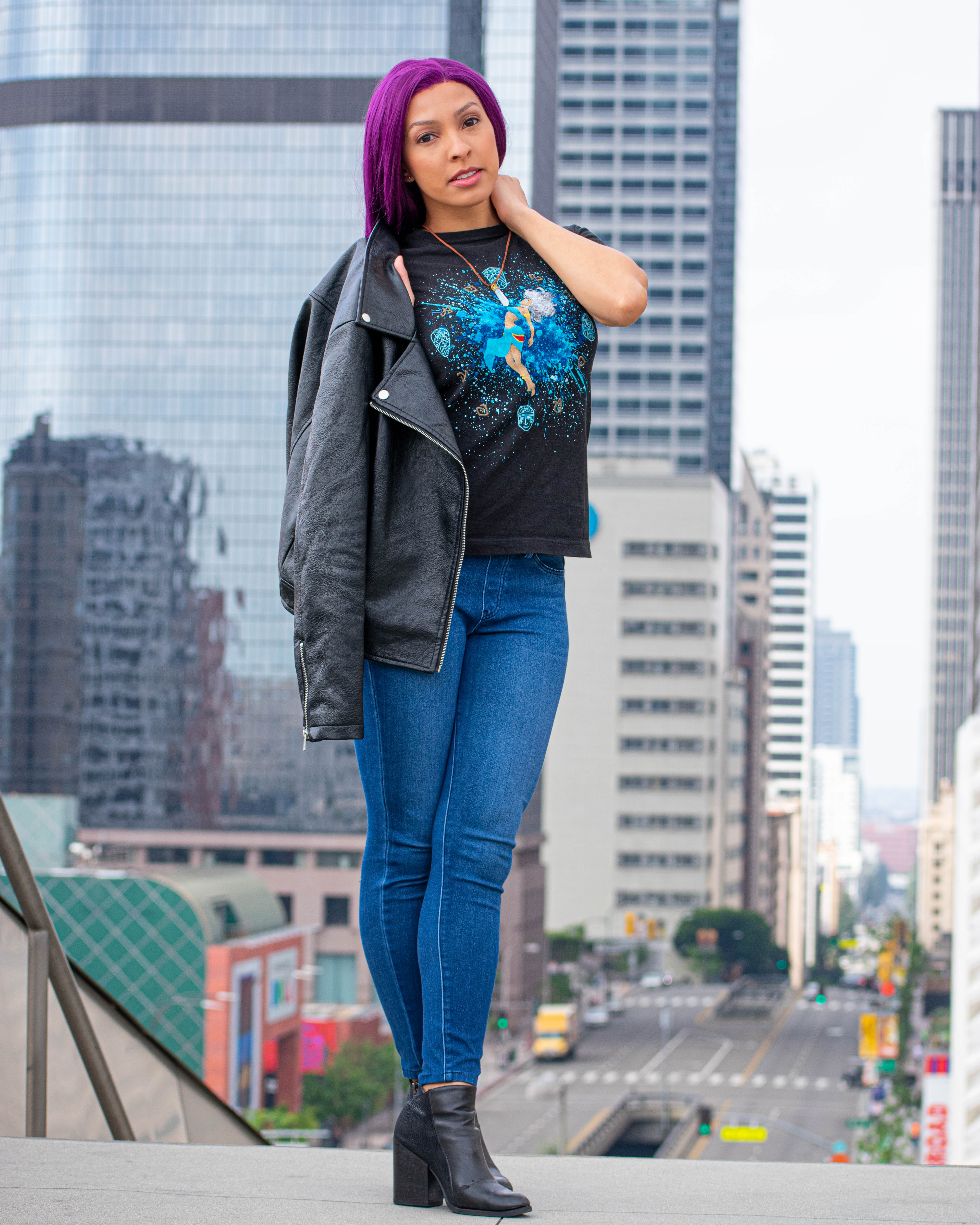 Utahime Cosplay pictured in a Kida inspired Tee Shirt and crystal necklace. She is wearing jeans and a black leather jacket. The Los Angeles Skyline is visible behind her.