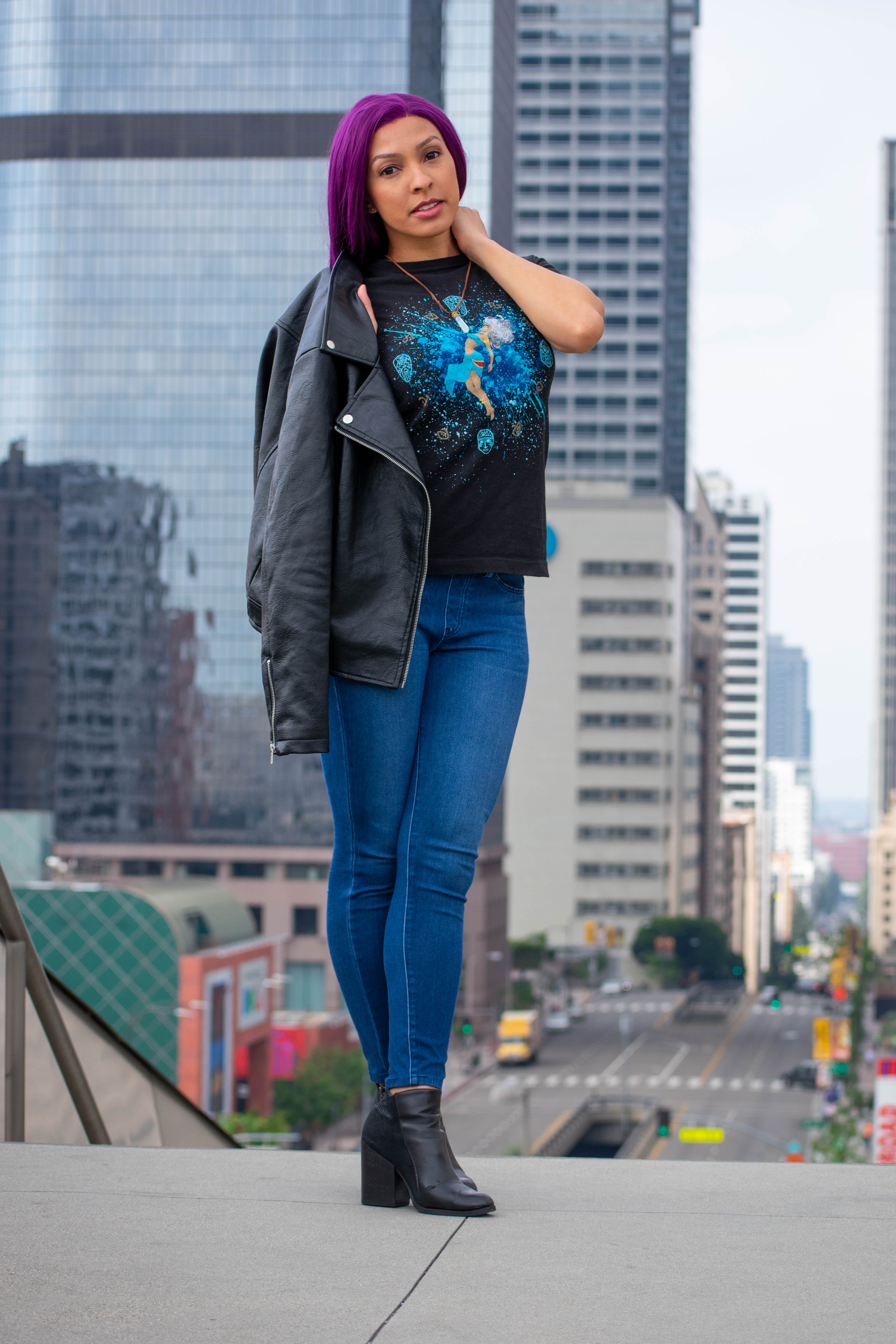 Utahime Cosplay pictured in a Kida inspired Tee Shirt and crystal necklace. She is wearing jeans and a black leather jacket. The Los Angeles Skyline is visible behind her.