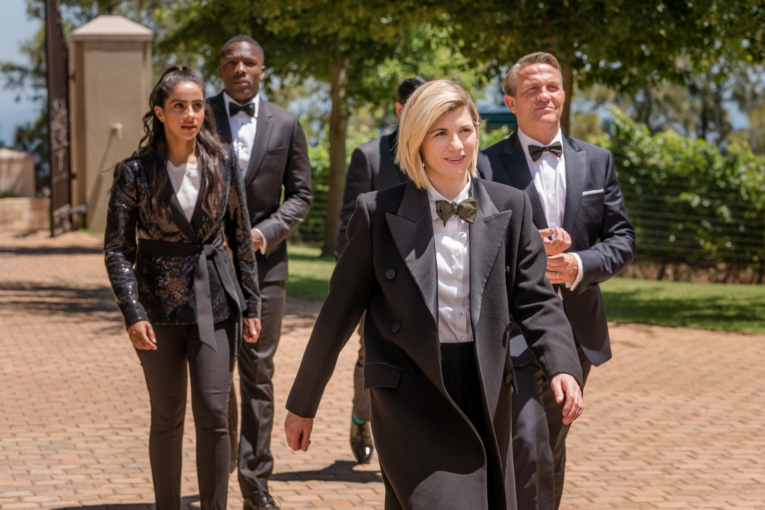 Photo of the cast of Doctor Who walking. They are wearing Tuxedos.