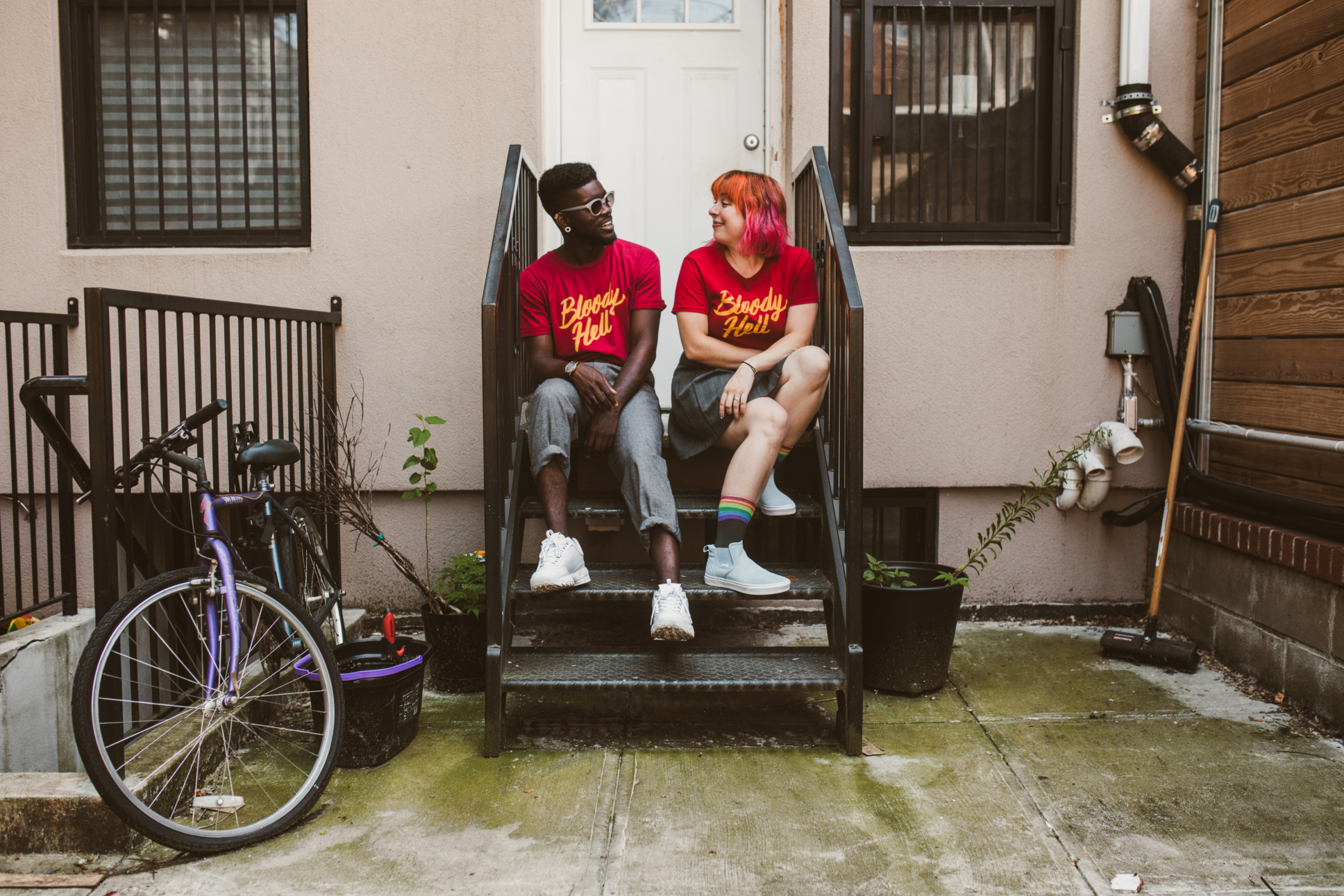 Jordan and her friend sit on porch steps wearing matching shirts that say "bloody hell" 