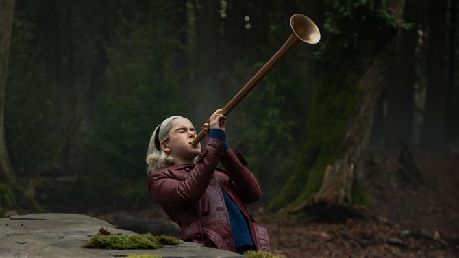 Sabrina standing in the wood blows Gabriel's Horn