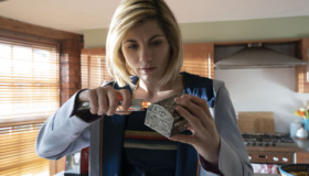 Jodie Whittaker as The Doctor holds her sopnic screwdriver to a small metal box and scans it .