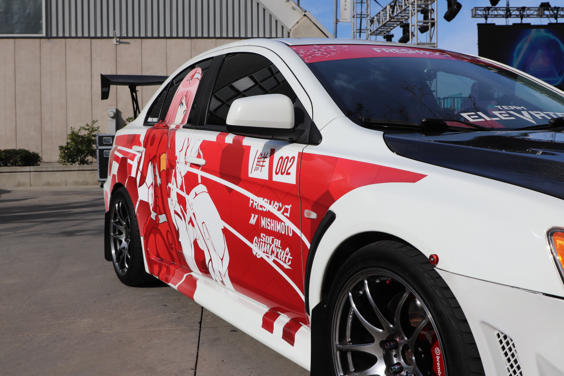 Photo of a car. The car is wrapped in anime and racing tribute.