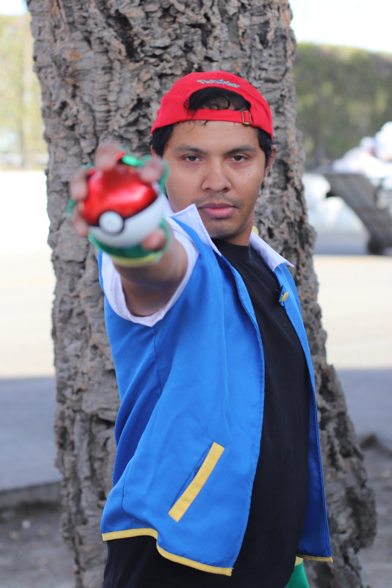 Cosplayer dressed as Ash Ketchum is holding a pokeball out towards the camera