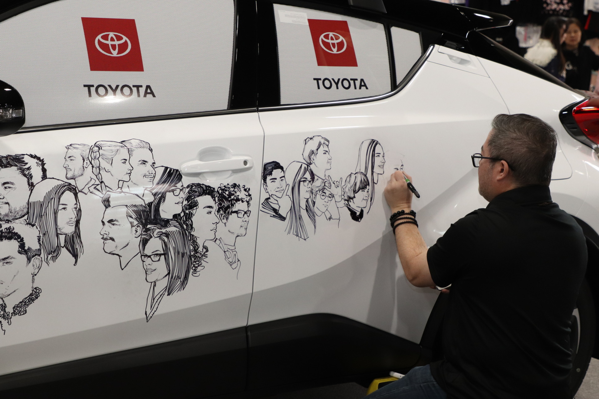 an artist draws peopl'e faces on a Toyota car