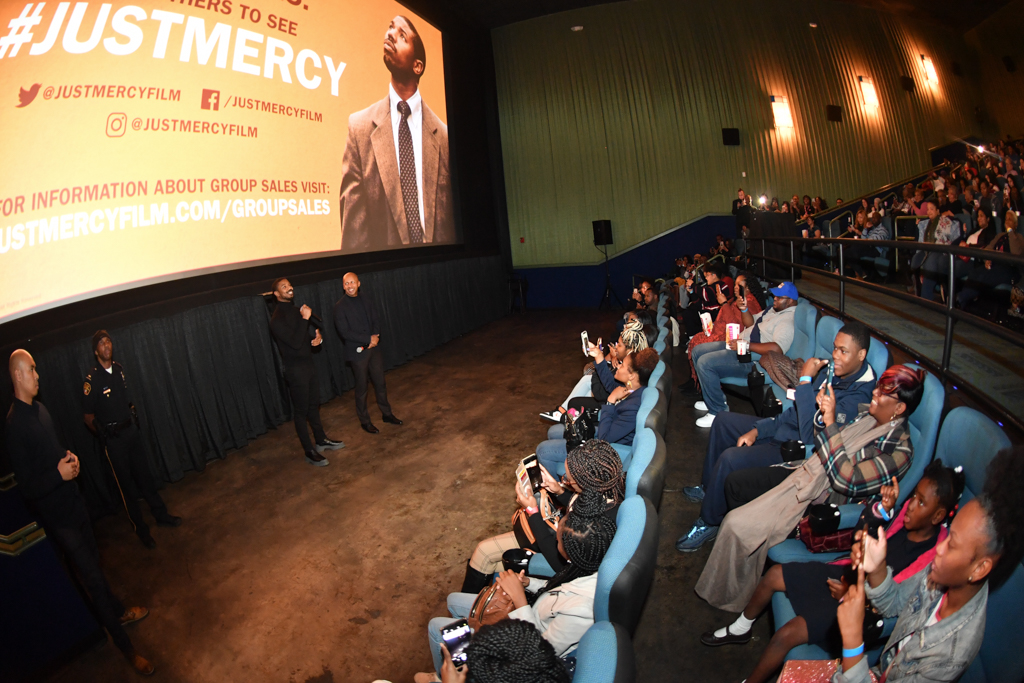 Photo is of people seated in a movie theater. On the screen is the promotional poster of the film Just Mercy