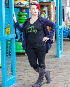 model is standing near an arcade on a beach pier in front of a shop wearing a tshirt that says Defy Gravity