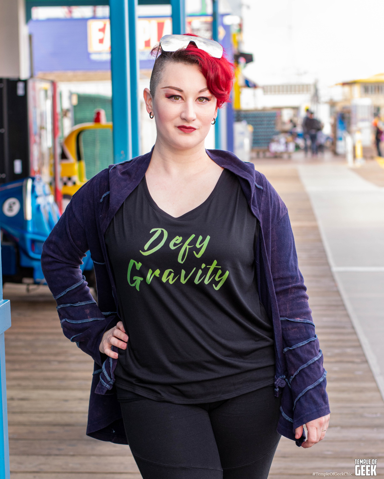 model is standing on a beach pier in front of a shop wearing a tshirt that says Defy Gravity