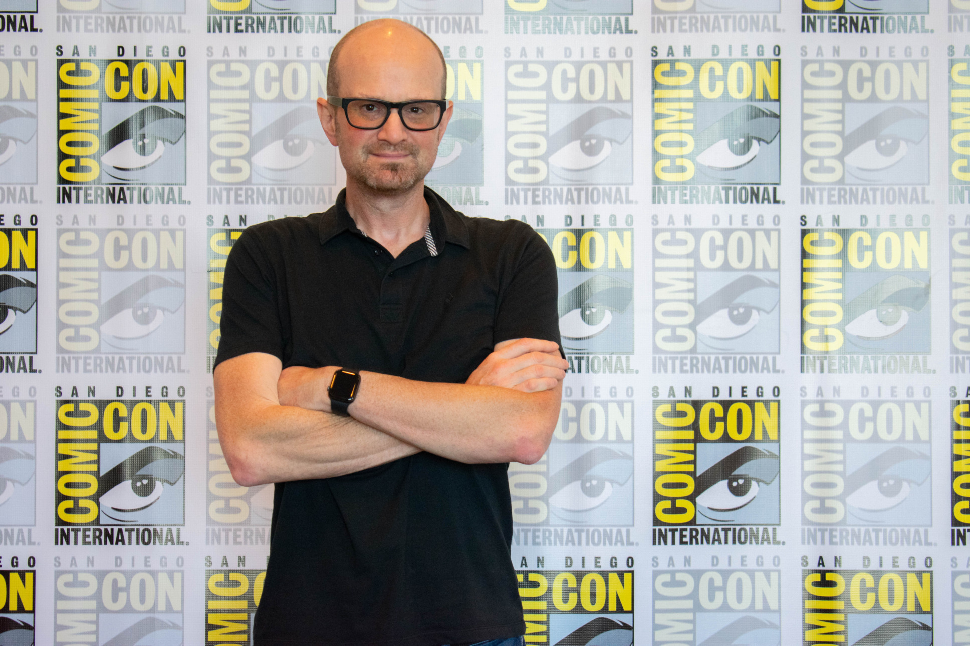 Brian Volk-Wess Founder and CEO of The Nacelle Company poses with his arms crossed in front of a banner at San Diego Comic Con 2019. The banner is a photo backdrop with the SDCC logo.