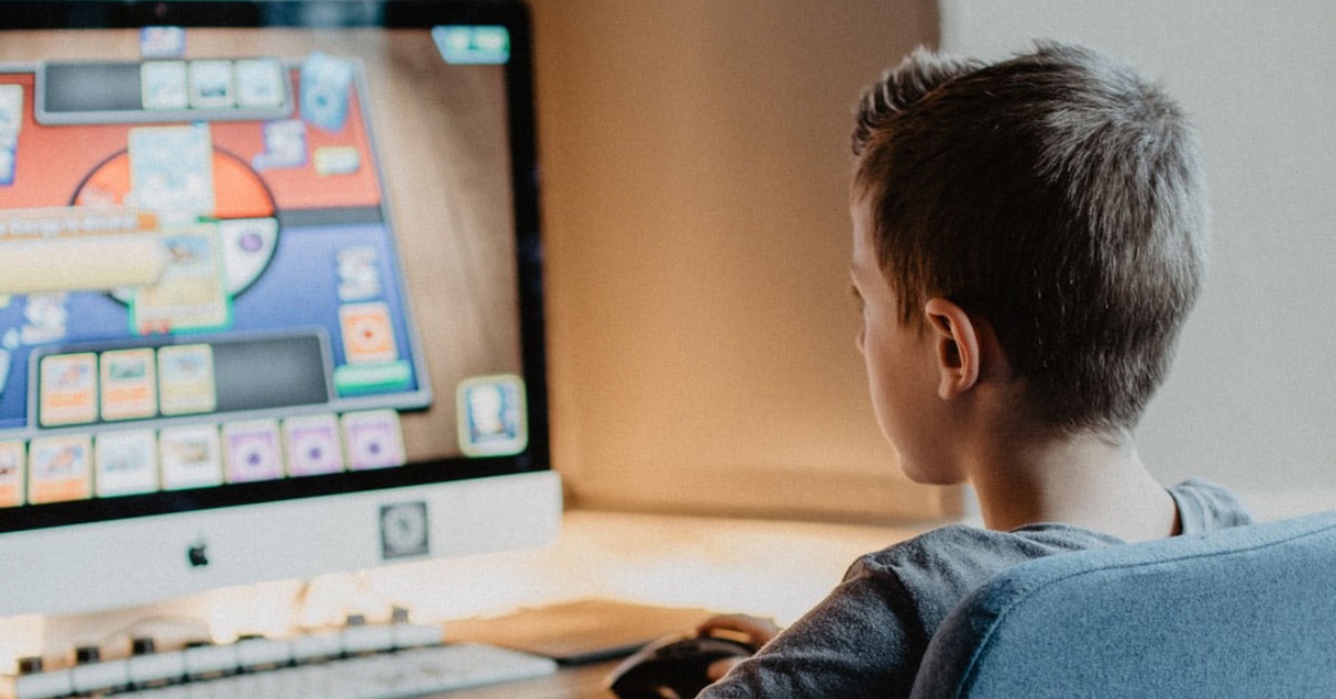 a child sits a desk, infron of a computer playing a pc game