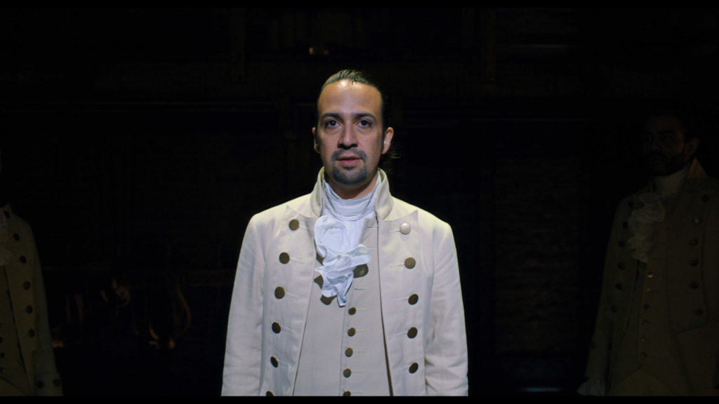 Lin Manuel-Miranda as the Title character of Alexander Hamilton. He is on stage in an all white colonial area costume