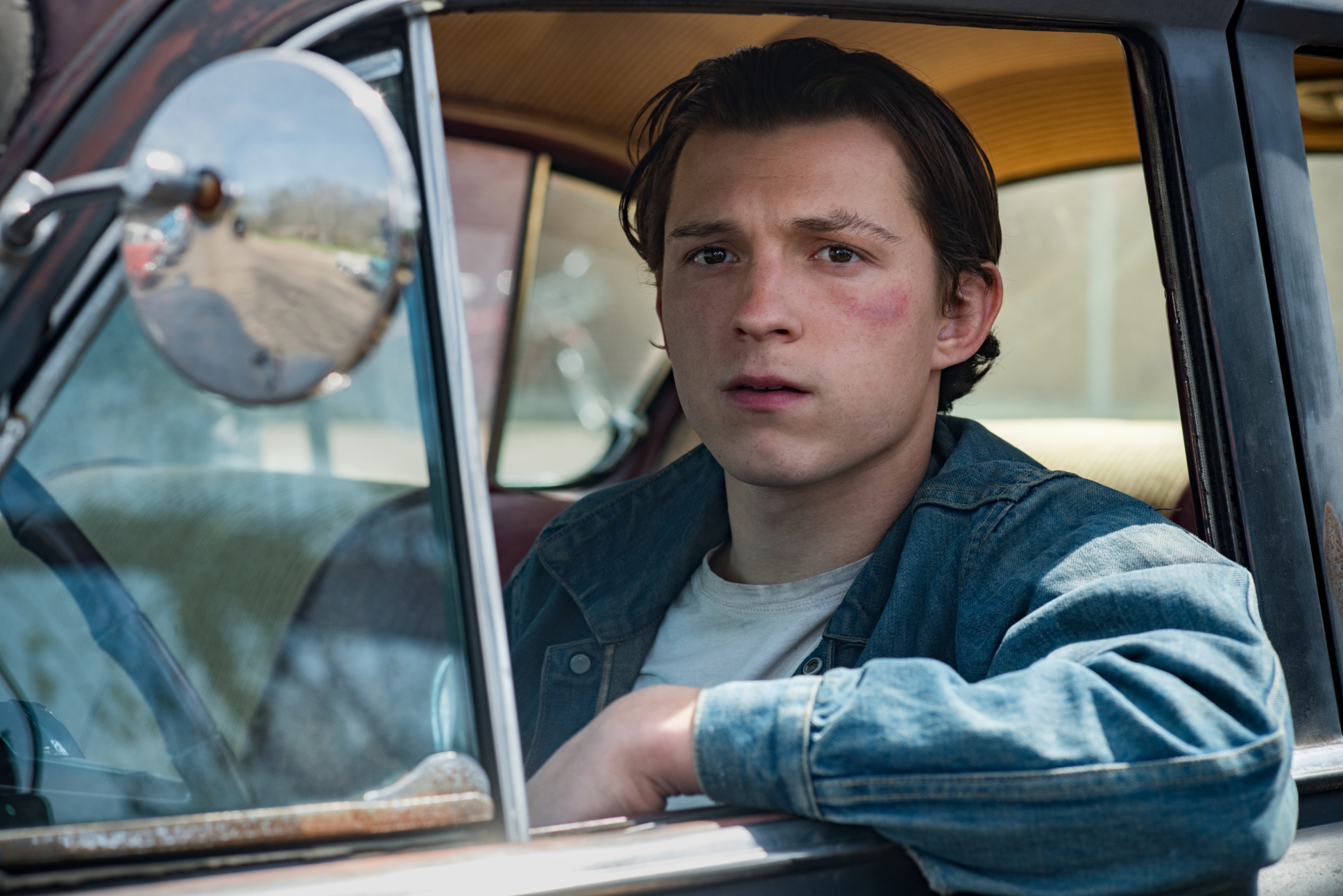 Tom Holland sits in the driver side of a vintage 1960s car looking out the window