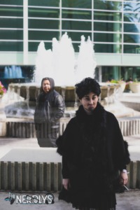 Rachel Ly (Klaus Cosplay) and Chris Ly (Ben Cosplay) stand near a water fall at a convention center. They are dressed as Ben and Klaus from Season 1 of the Umbrella Academy