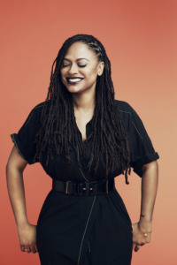 Ava DuVernay stands with arms at her side, eyes closed and a big smile as she poses for a photo.