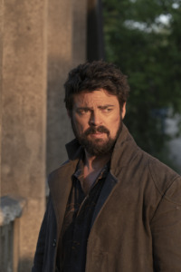 Billy Butcher (Karl Urban) stares off screen. The light from the sunset is hitting his face,