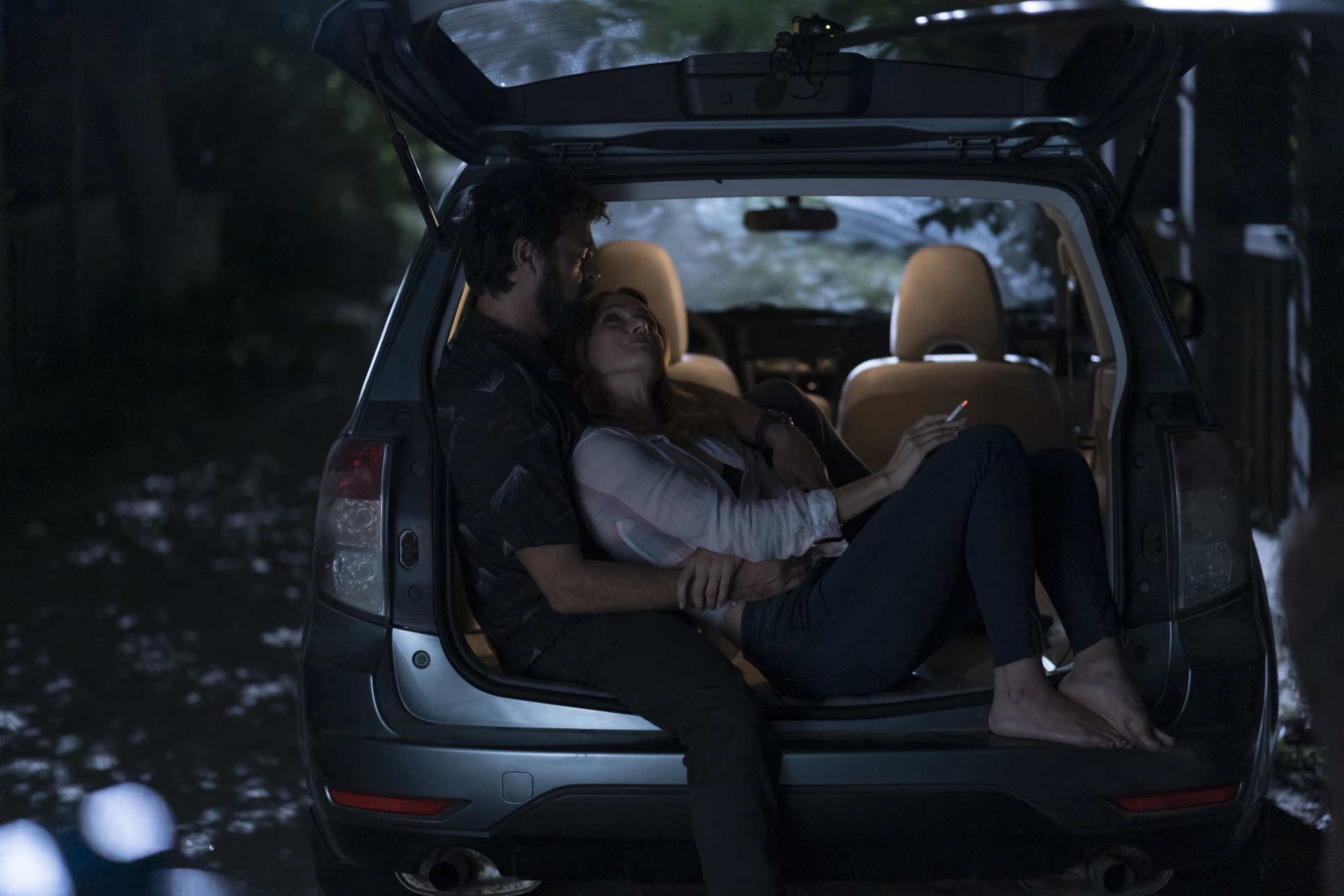 Becca (Shantel Van Santen) and Butcher (Karl Urban) sit in the hatch back portion of Becca's car. They are holding one another as Becca smokes a cigarette. She looks up at Butcher lovingly.