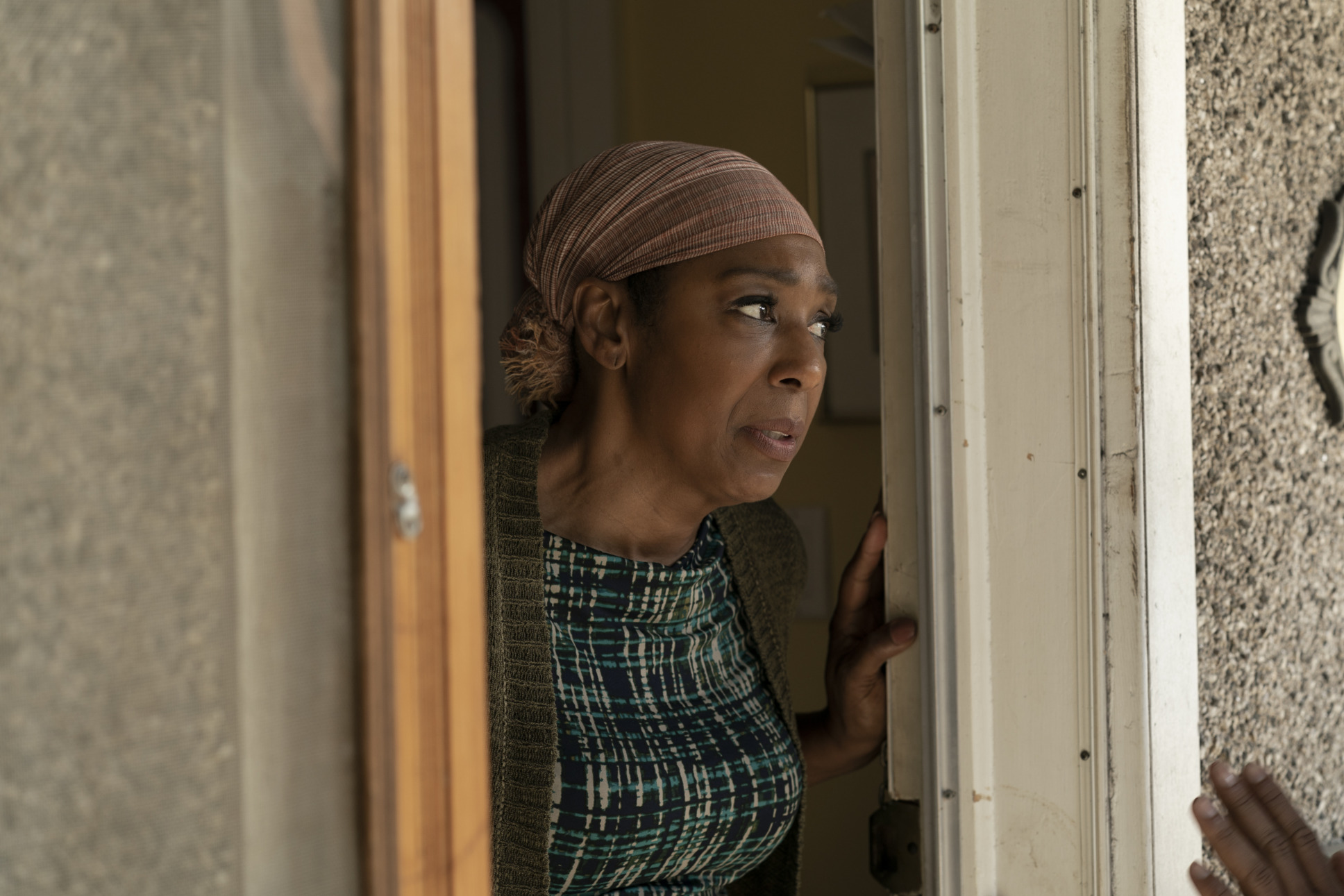 a woman looks out the front door from iside her home. She is listening toi someone speak to her from the porch