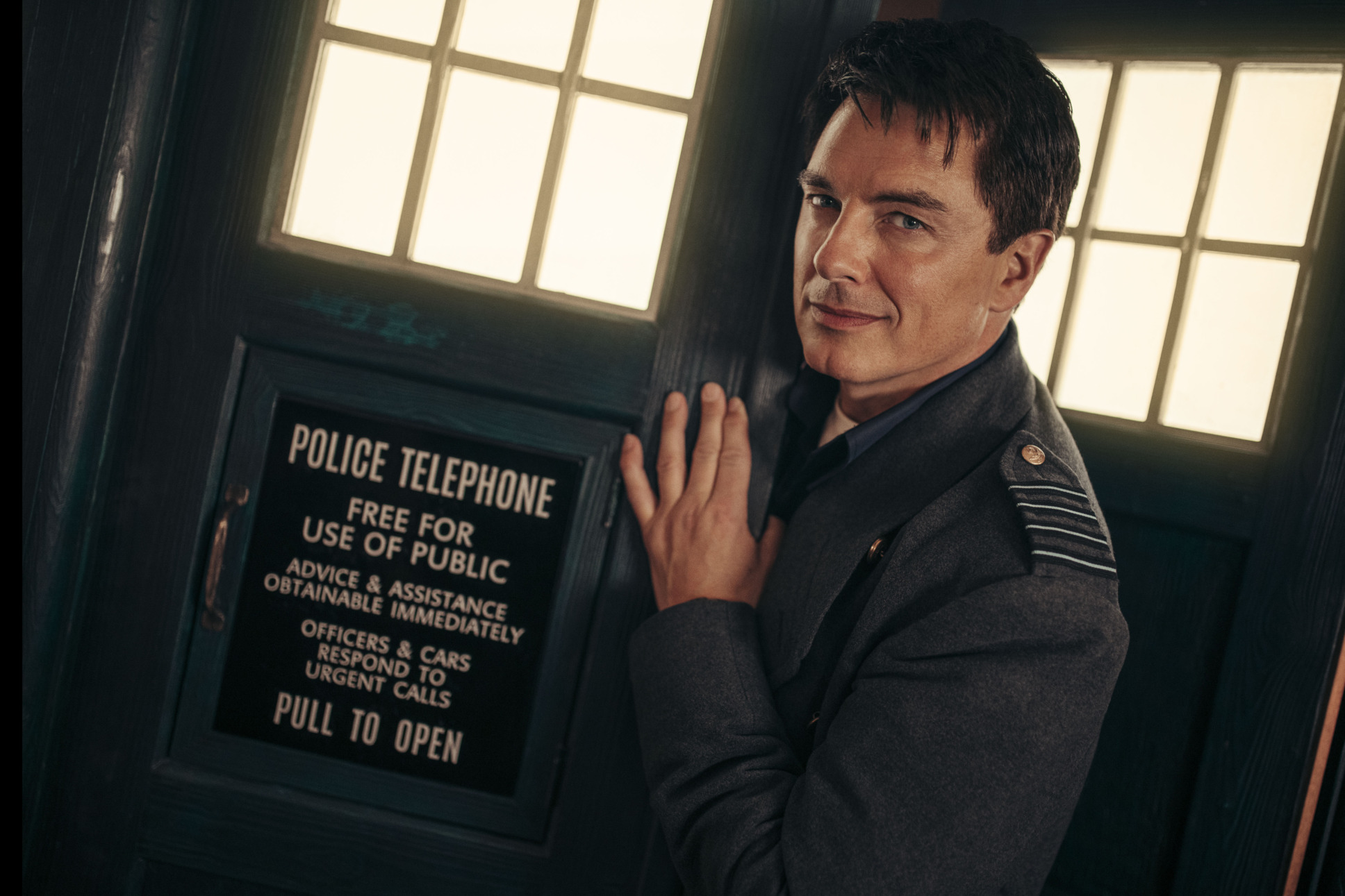 John Barrowman as Captain Jack Harkness standing in front of the TARDIS doors