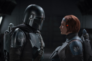 Man wearing Star Wars Mandalorian suit (Pedro Pascal) and women with short red hair (Katee Sackhoff) stare at each other. Katee Sackhoff has attributed her career to being a fangirl, allowing her to star alongside other Sci Fi actors