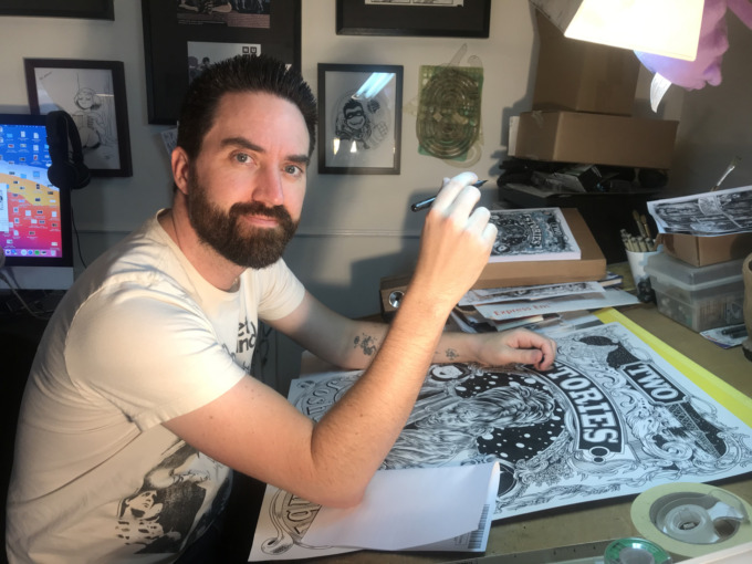 Joshua Kemble sits at his drawing table working on a poster of Two Stories: Book One