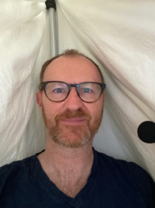 A picture of Mark Gatiss recording for Big Finish at home- he has a michrophone and a large blanket behind him to control the sound in the room