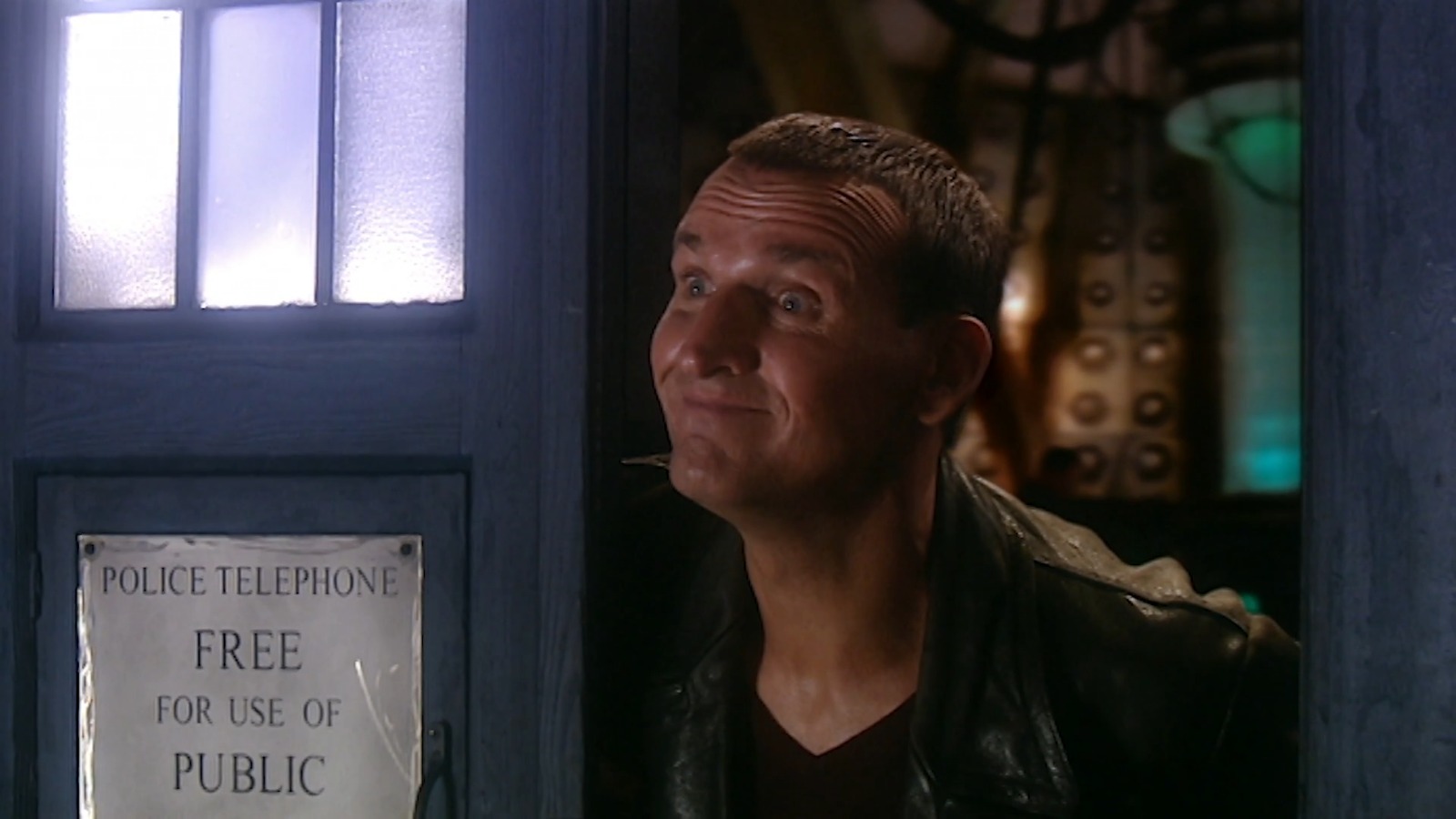 The 9th Doctor standing in the door frame of his TARDIS, smiling at Rose