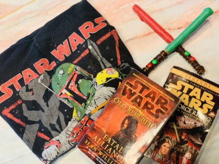 Photo includes a folded Boba Fett Star Wars Tshirt, a Green Pretzel Lightsaber and a Red Pretzel Lightsaber. There are also two Star wars novels in the photo, "The Old Republic" and "The Force Rising" 