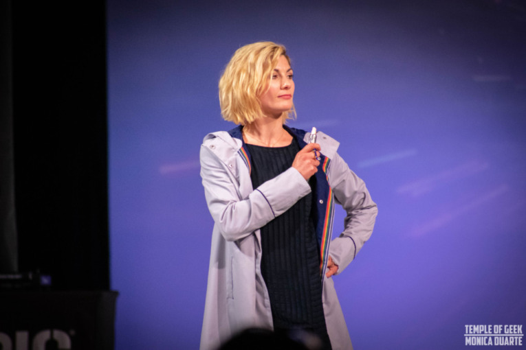 Jodie Whittaker wears a 13th Doctor Coat made by Her Universe and holds a sonic screwdriver on the stage of the 2018 Her Universe Fashion Show