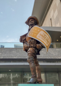 Statue of Sir Walter Raleigh outside of the Raleigh Convention Center, with a large bandage across his arm that reads "I got my VACCINE for COVID-19!"