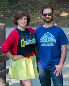 A smiling couples model ShimmerPop Shop's unique Disney tees and totes on a bridge. 