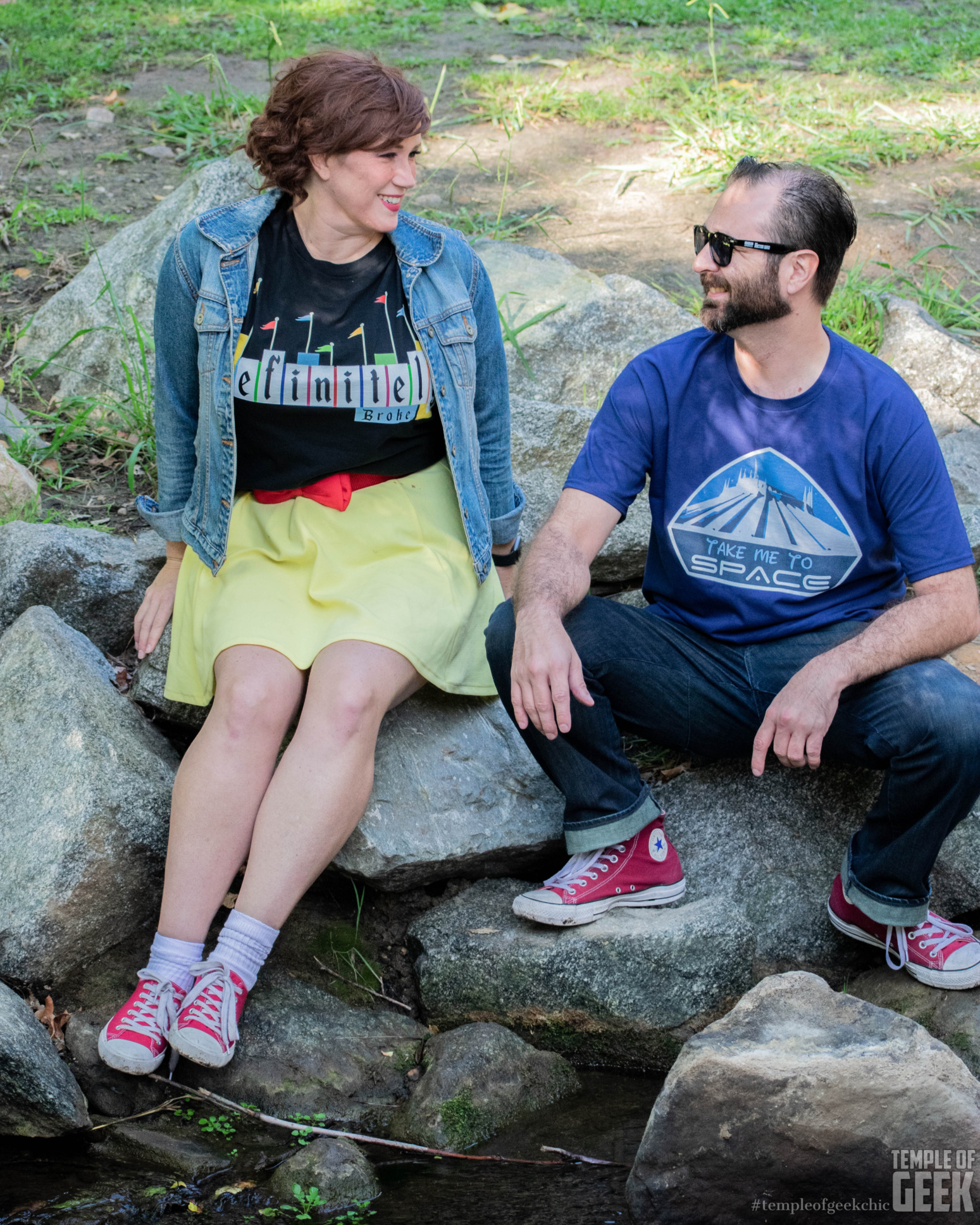 Two models sit on rocks and smile at each other, wearing Disney tees.