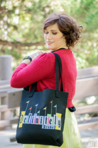 A model carries a Disney-themed tote bag that reads "Definitely Broke." 