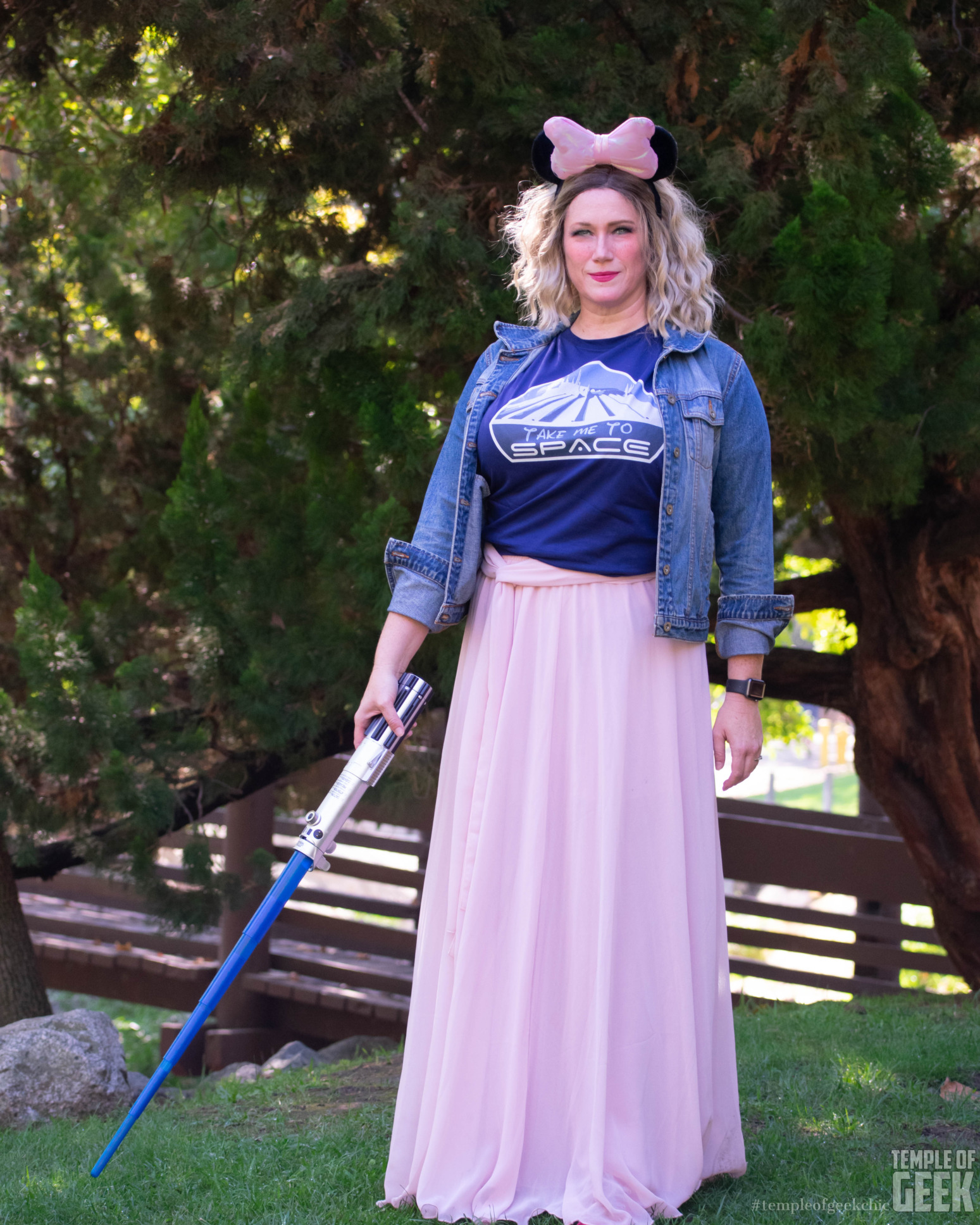 A model with a lightsaber wears Minnie Mouse ears, a Disney tee, and a flowy pink skirt.