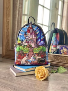 A Beauty and the Beast themed mini backpack from Loungefly rests atop a stack of books next to a yellow rose. 