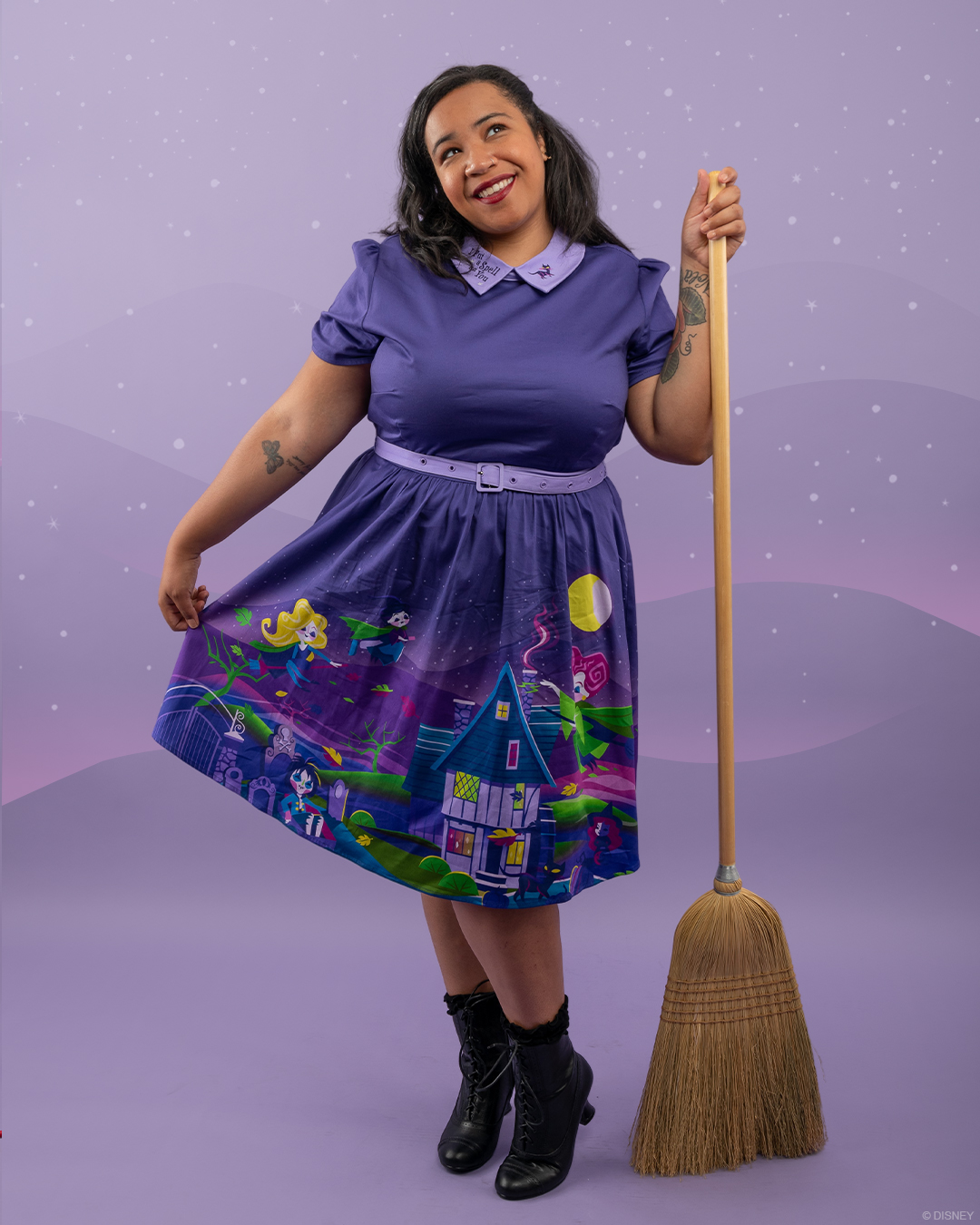 A model holding a broom shows off the skirt of a Hocus Pocus themed dress from the Loungefly Stitch Shoppe brand.