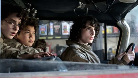 L-R Mckenna Grace as Phoebe. Finn Wolfhard as Trevor and Logan Kim as Podcast sit in the Shostbuster vehicle, the Ecto-1