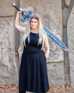 A model holds a sword over her head while wearing the black Longsword Dress.