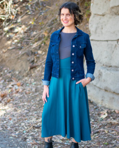 A model wears a denim jacket over the gray and teal Longsword Dress.