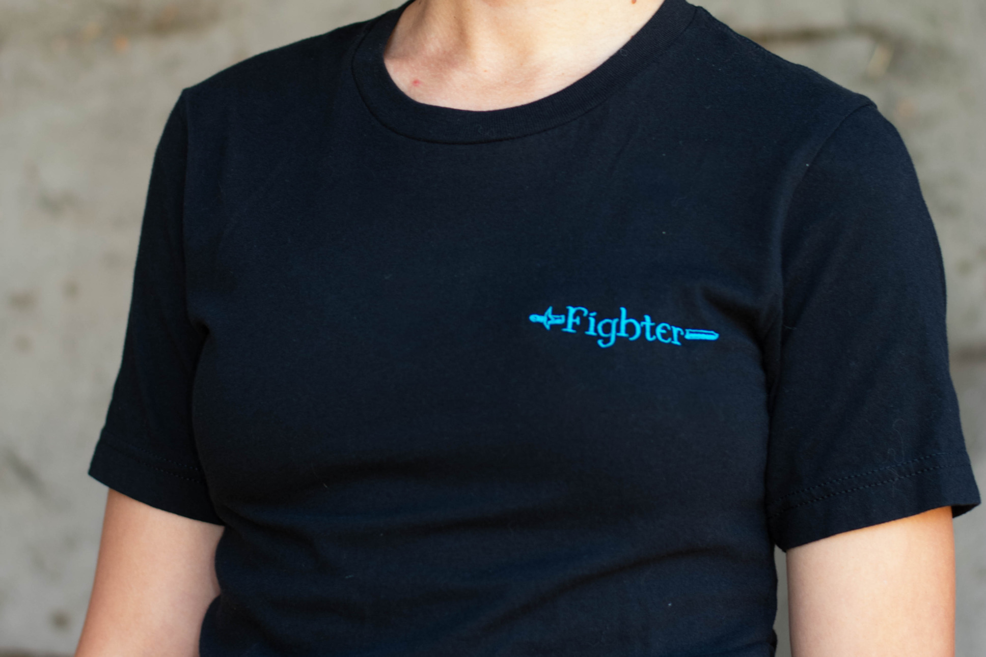 Closeup of an embroidered emblem with a sword and the word Fighter on a tee.