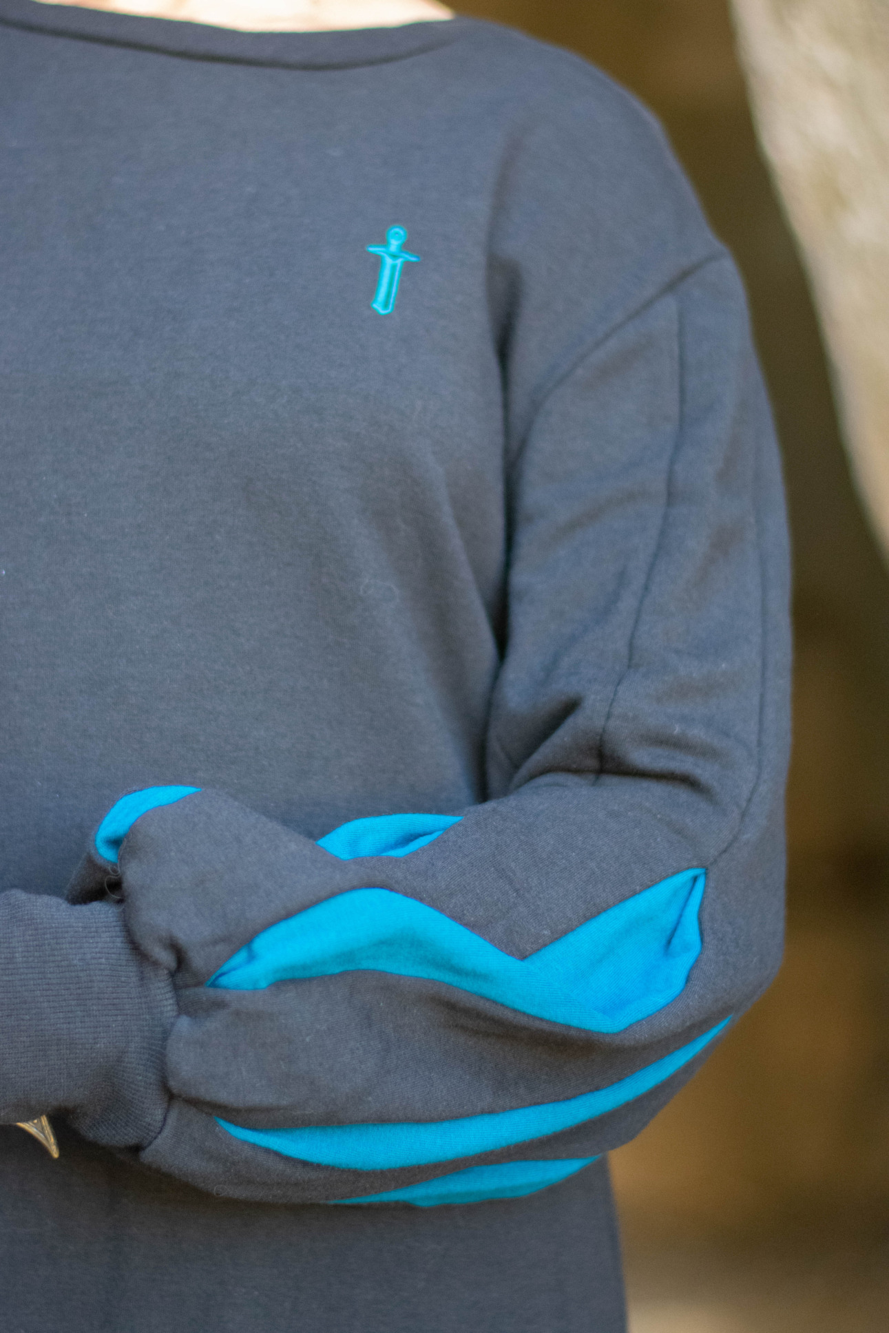 Closeup of a black pullover featuring bishop sleeves with blue inserts and an embroidered sword emblem by D&D fashion brand Guild Party.