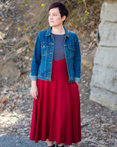 A model wears a denim jacket over a red and gray Longsword Dress by D&D fashion brand Guild Party.