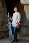 A model holds a massive sword and wears a gray pullover with bishop sleeves.