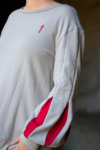 Closeup of a gray pullover with bishop sleeves with red inserts and an embroidered sword emblem by D&D fashion brand Guild Party.